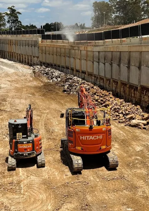 Two Hitachi excavators on a bulk excavation beside a shoring wall