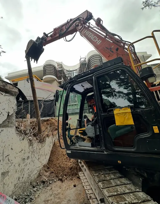 Mustang's Hitachi demolishing a concrete wall beside a building
