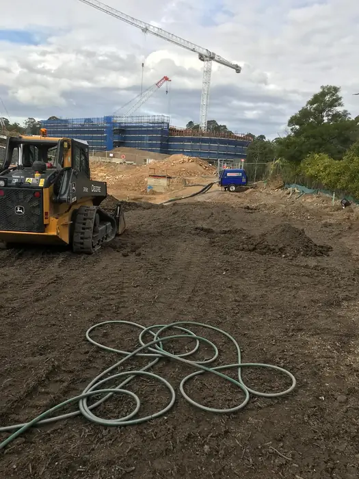 Skid steer preparing an open earthworks site beside a building project